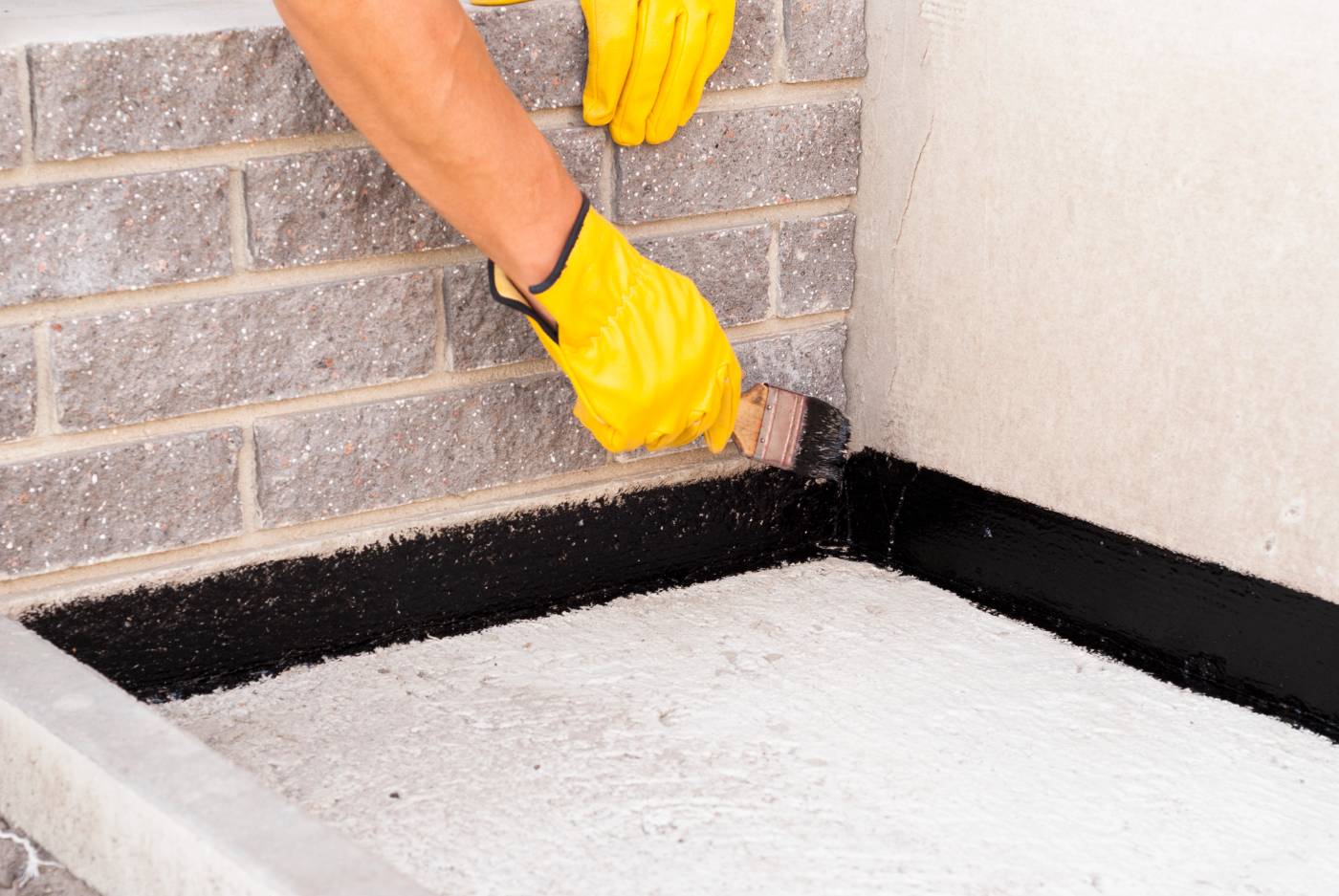 How Much Does It Cost to Waterproof Your Basement in Canada? 7 Worker applying bitumen mastic to foundation of building - How Much Does Basement Waterproofing Cost in Canada?